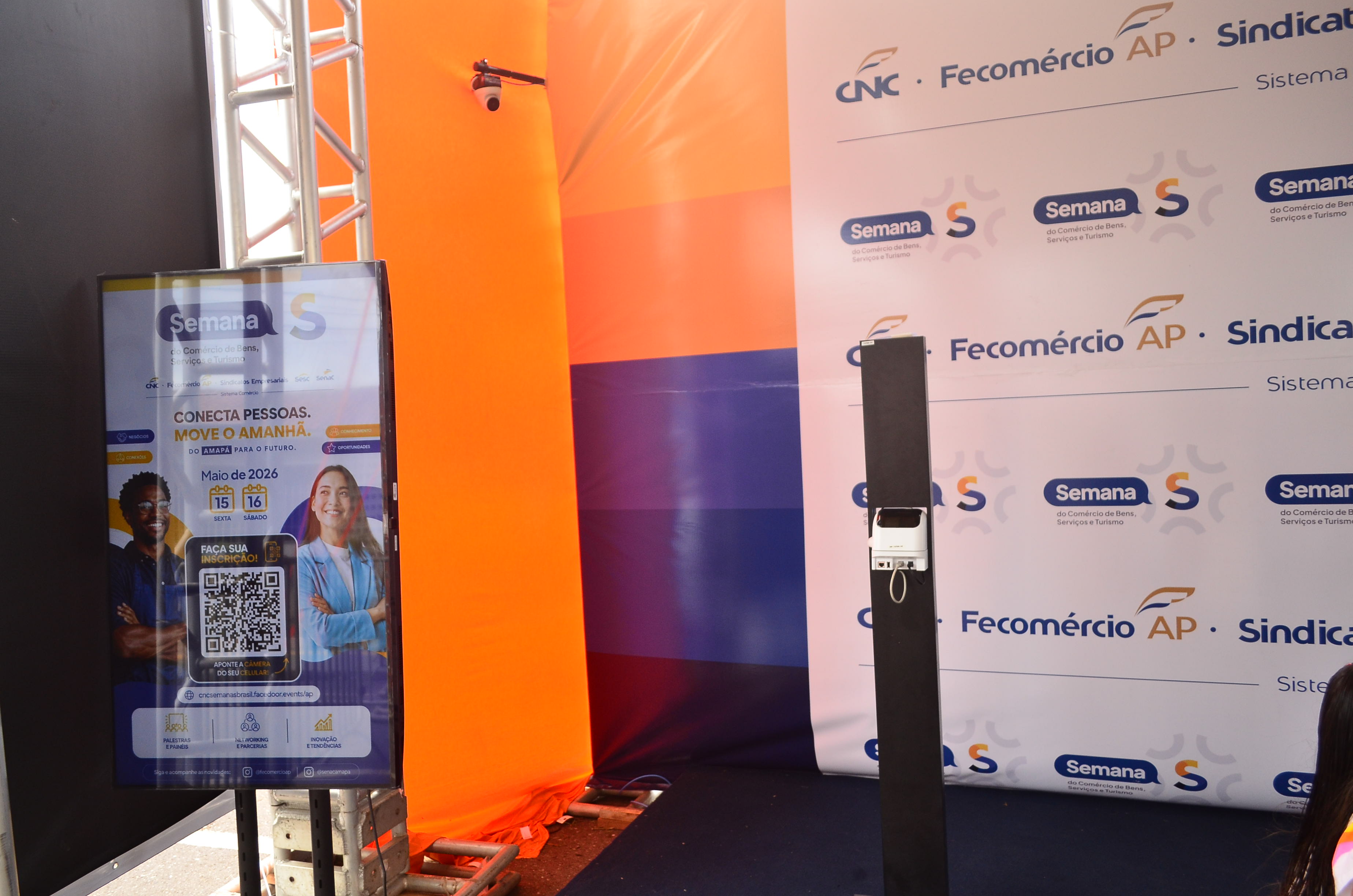 Totem da Facedoor em frente ao painel do evento com as marcas CNC, Fecomércio AP e Semana S