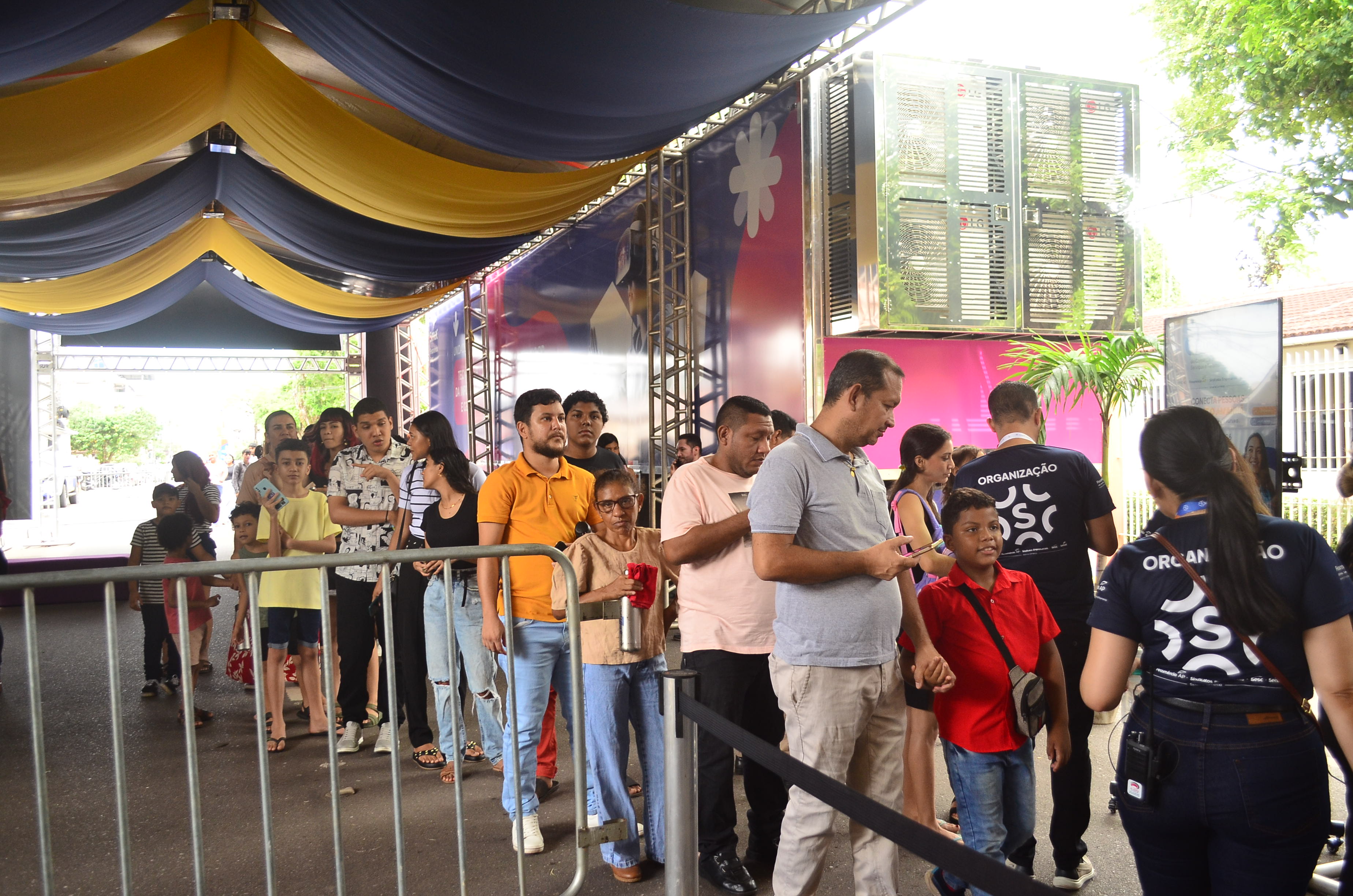 Fila de participantes atendida no balcão de credenciamento, com a equipe da organização operando as estações
