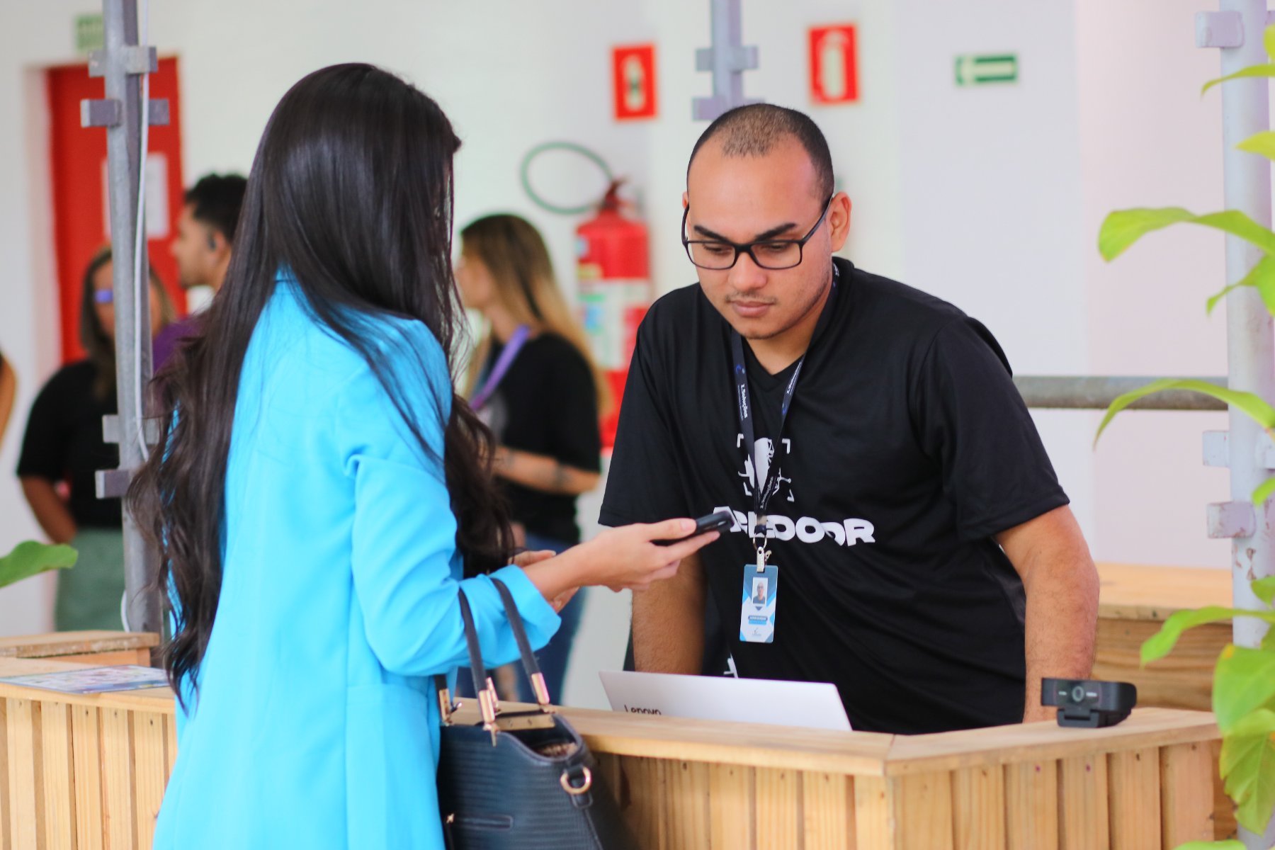 Técnico da Facedoor atende uma participante no balcão de credenciamento, com laptop e câmera de verificação